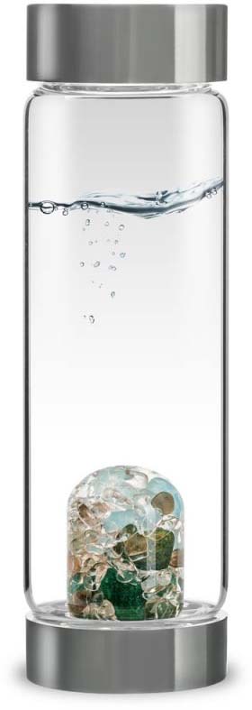 Transparent ‘ VitaJuwel ’ ViA drinking bottle made from borosilicate glass with silver caps. Contains clear, gently agitated water with tiny bubbles. At the bottom is a glass insert containing gemstones in shades of green, blue and light brown.
