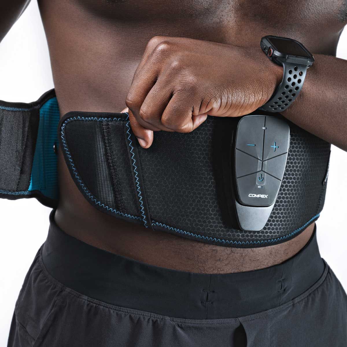 A man puts the black Compex CoreBelt 5.0 muscle stimulation belt around his waist and adjusts it. The belt, which features blue stitching and a detachable control unit, is designed for EMS training of the abdominal and back muscles.