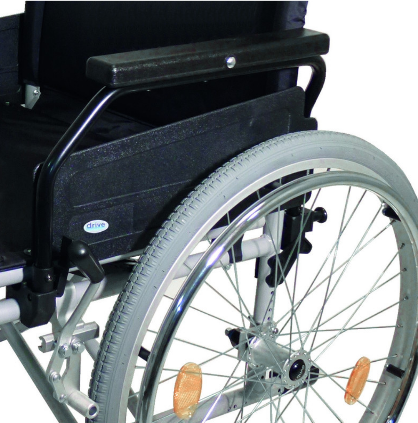 Primo piano del lato destro della sedia a rotelle: bracciolo imbottito nero e grande ruota posteriore con pneumatico grigio chiaro, raggi argentati, cerchio lucido e catarifrangente arancione. Pannello laterale nero con logo "drive".