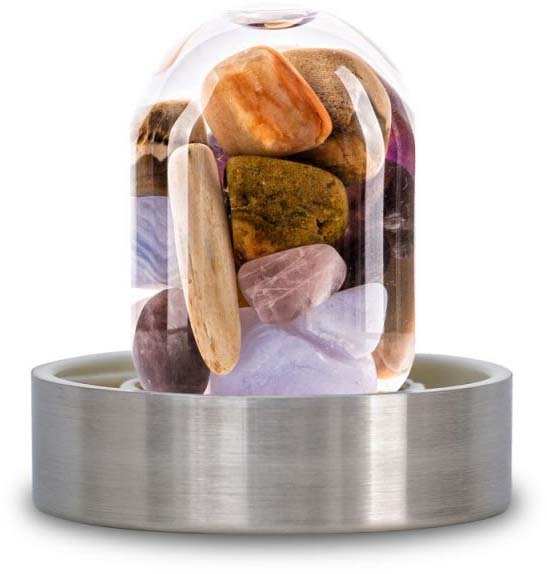 A transparent glass gemstone insert for water bottles, filled with polished, coloured stones: purple amethyst, pale pink rose quartz and clear rock crystals. The insert is set in a round, silver-coloured metal base.