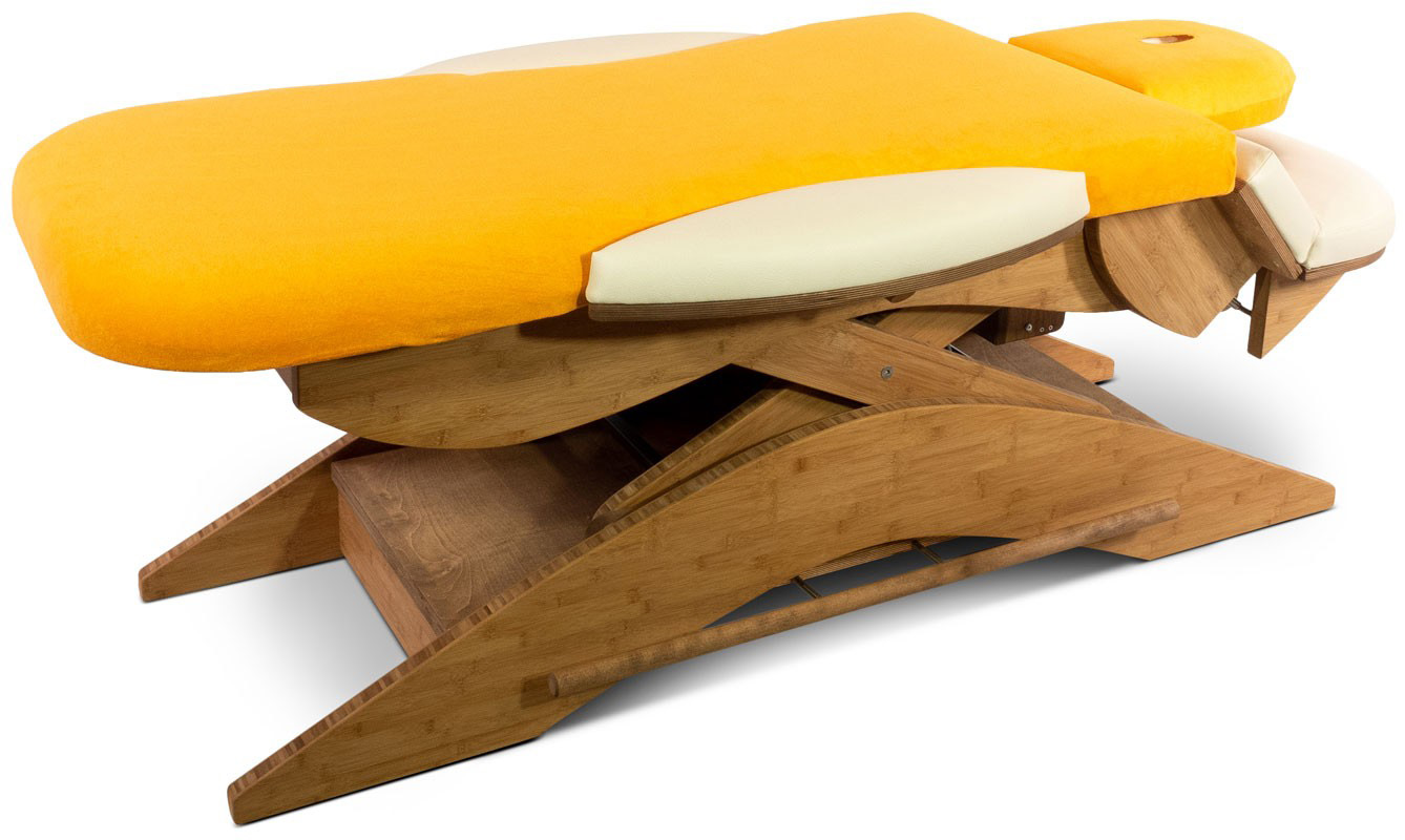 Professional treatment couch with a bright orange cover and cream-coloured side cushions. Ergonomically shaped lying surface and sturdy, curved base made of light-coloured wood for stability and adaptability. Optimised for therapy.