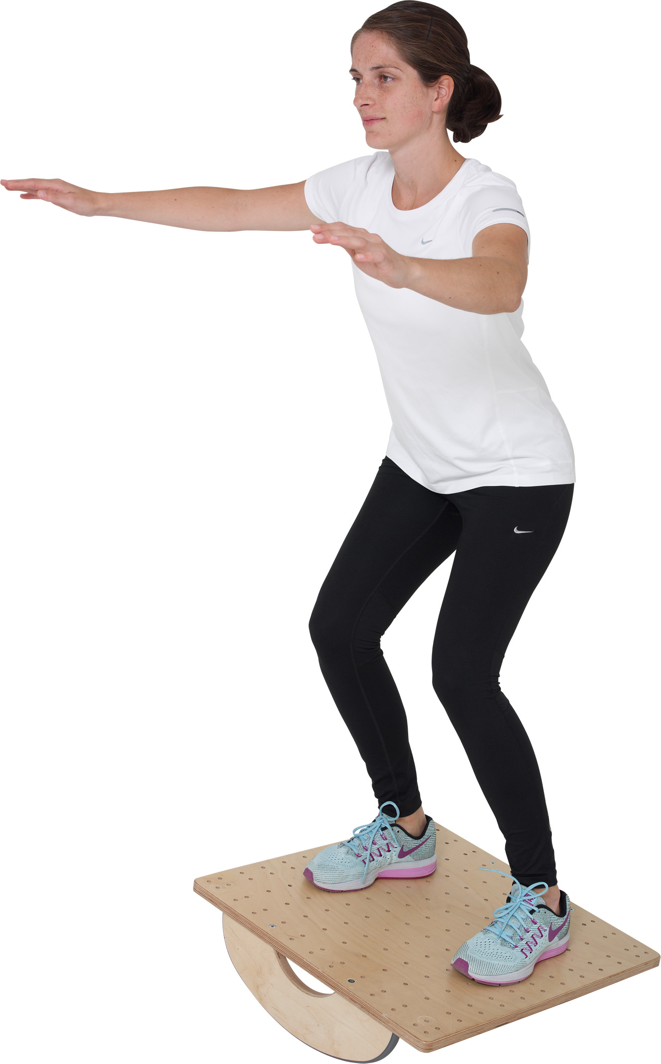 A woman in sportswear is exercising on a Pedalo PT balance board. She is standing in a slight squat, with her arms outstretched to maintain her balance. The wooden board rocks gently as she works on improving her stability for physiotherapy exercises.