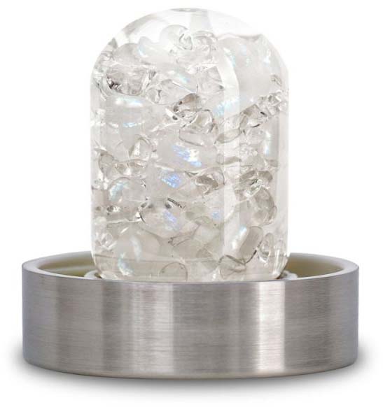 Cylindrical glass insert with small, clear gemstones such as rock crystal, amethyst and rose quartz, set in a round brushed stainless steel ring. The stones show iridescent reflections and are intended to revitalise water in a bottle.