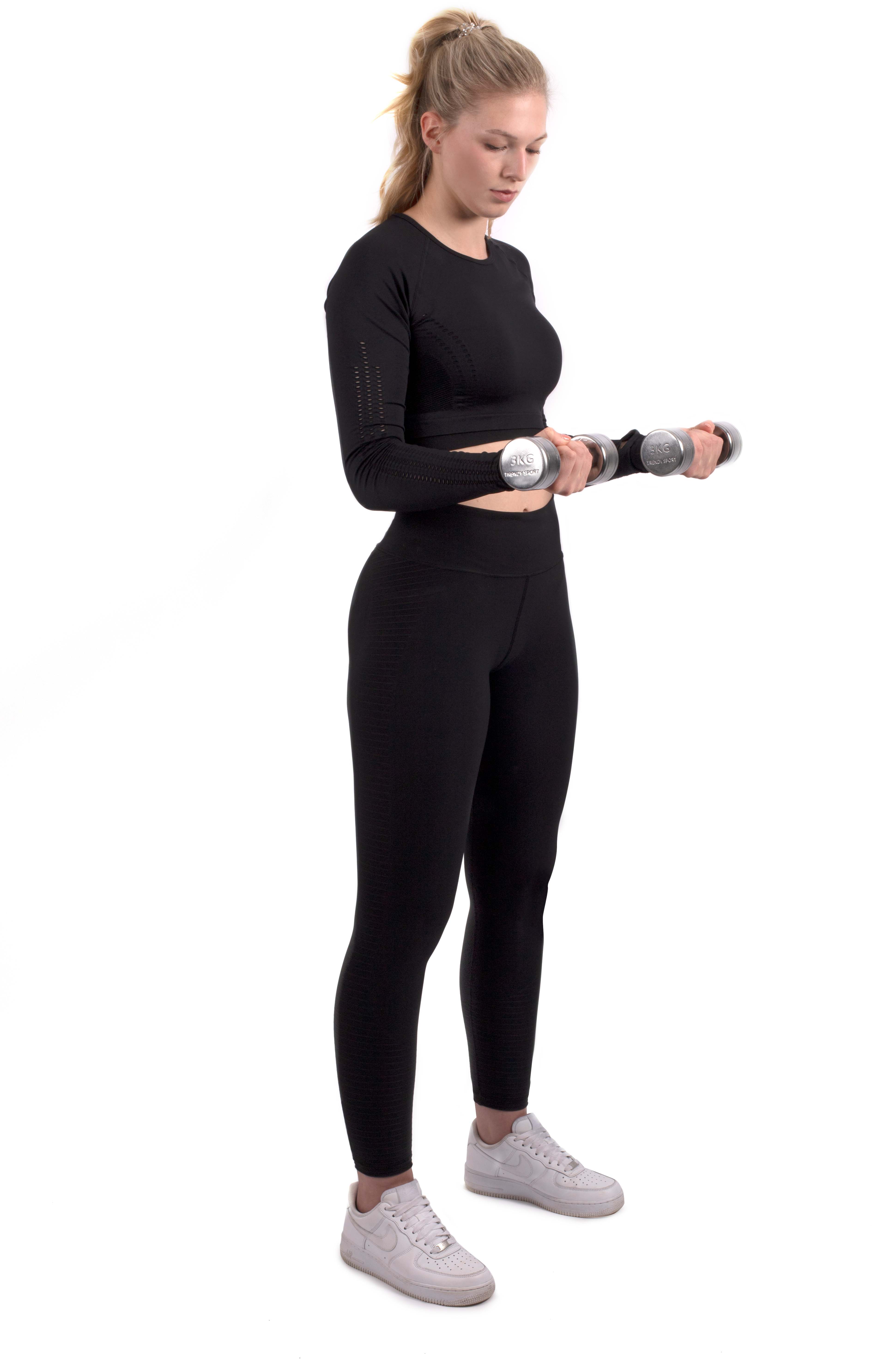 Jeune femme blonde en queue de cheval, en tenue de sport noire, tenant deux haltères chromés argentés « 3KG Trendy Sport ». De profil, elle regarde les poids avec concentration, prête à faire du fitness.