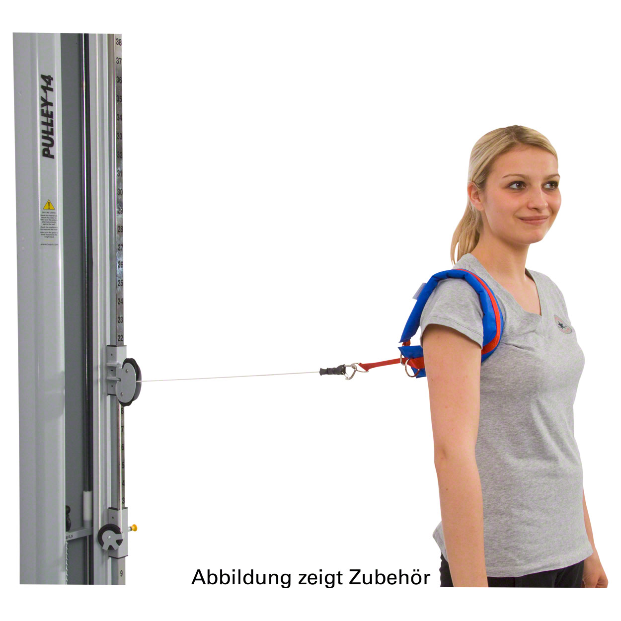 A young woman with a blonde plait and a grey T-shirt is wearing a blue and red padded rotation strap over her right shoulder, connected by a cable to a grey PULLEY 14 machine. She is looking to the right and preparing to do a shoulder exercise.