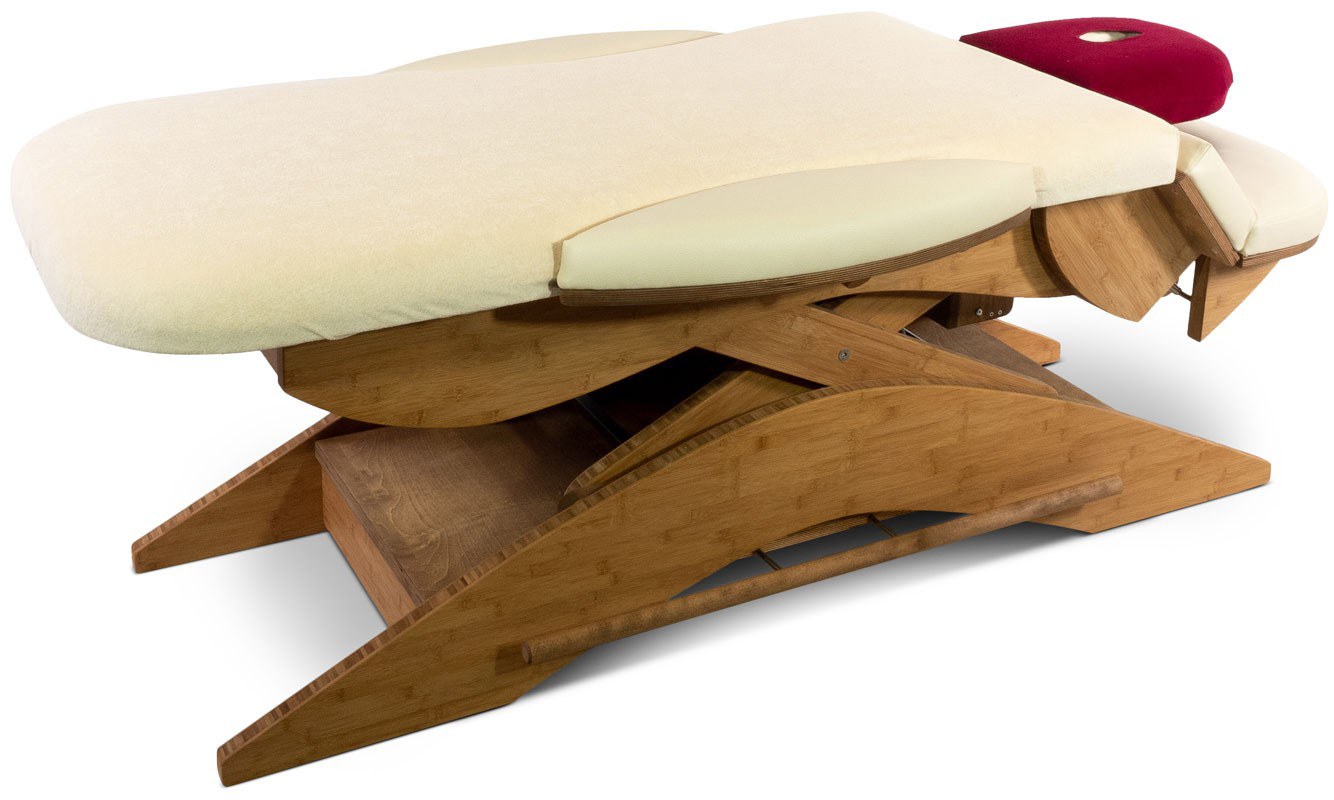 A light-coloured therapy couch with a curved wooden frame for stability. The lying surface has a soft, cream-coloured cover with side padding. At the head end is a red, padded neck support with a cut-out for the face.