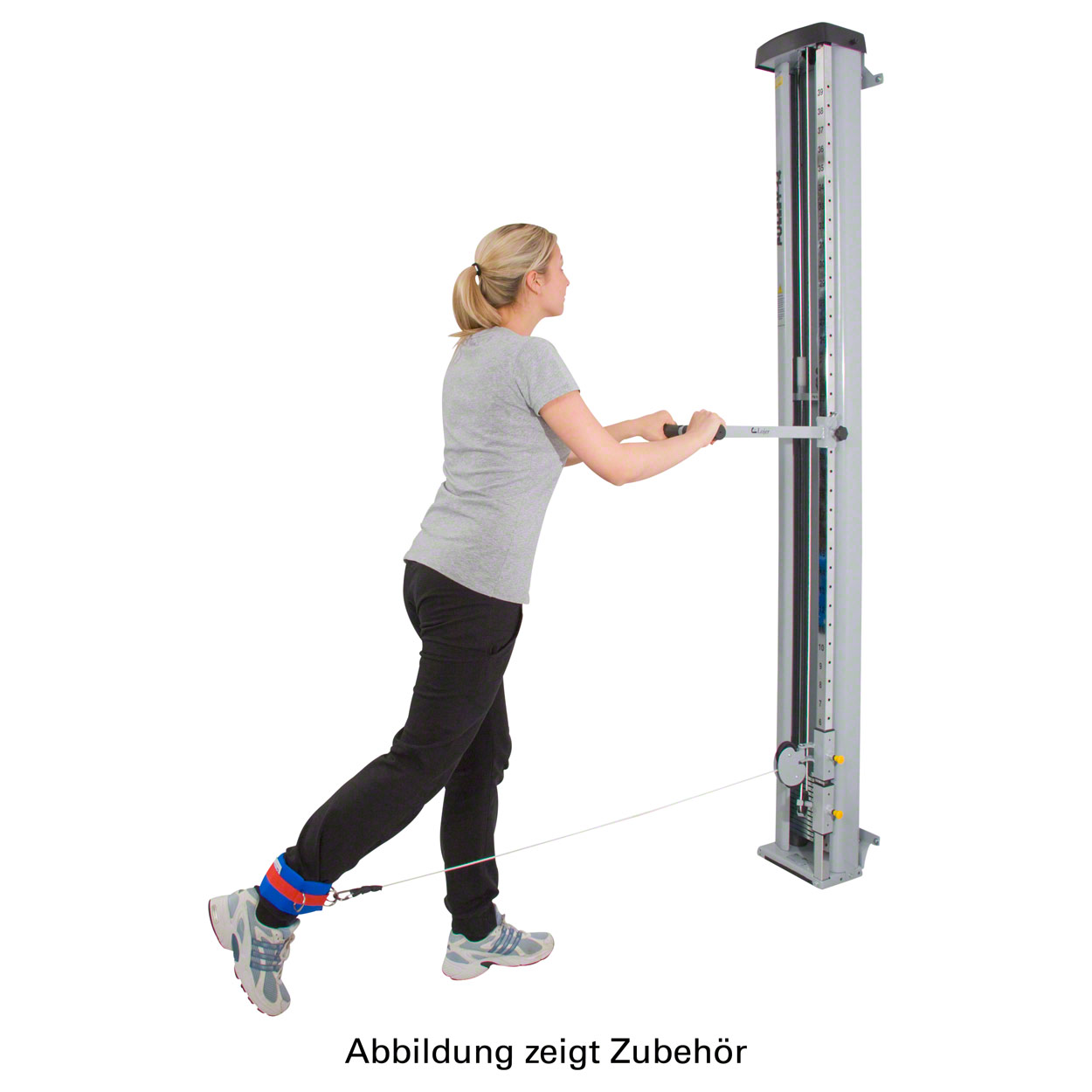 A woman in sportswear is training on the cable machine. She is holding a handle with both hands and is wearing a red and blue hand-and-ankle strap on her right ankle. She carefully extends her leg backwards to work her muscles.