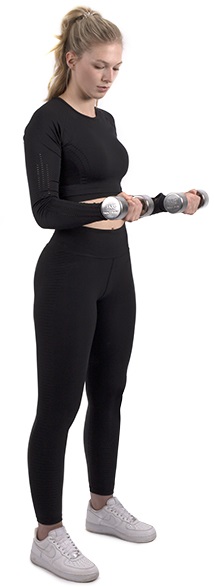 Une jeune femme blonde en queue de cheval, en tenue de sport noire, s'entraîne devant un fond blanc avec deux haltères chromés brillants. De face, elle fléchit les bras pour renforcer les muscles. Poignées striées.