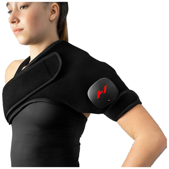A young woman is wearing a black massage belt around her left shoulder and upper arm. It fits snugly and features a small black unit with a red ‘H’ logo. It is designed to relieve shoulder pain or relax muscles and is adjustable with Velcro.