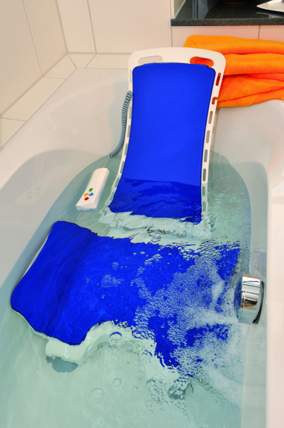 Un sollevatore per vasca da bagno Bellavita blu e bianco è installato nella vasca e parzialmente immerso nell'acqua per un bagno sicuro. Sul bordo c'è un telecomando impermeabile. Il rivestimento blu è visibile.