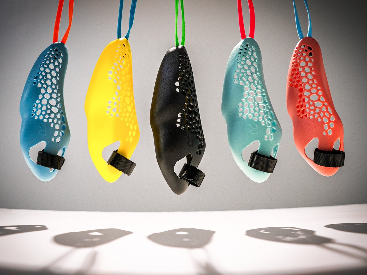 Cinq souris de course colorées, de forme ergonomique, sont suspendues en rangée sur un fond gris. Bleu clair, jaune, noir, turquoise et rouge corail, avec un motif alvéolé. Chacune est dotée d'une bande Velcro en bas pour la fixer à la main.