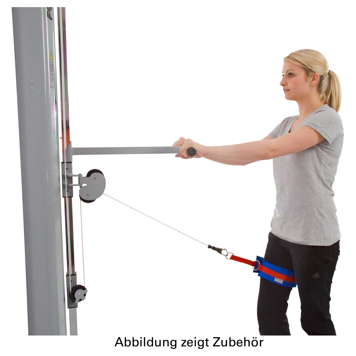 A blonde woman in sportswear is training on a cable machine. A padded red and blue strap is attached to her right thigh and connected to the cable. She is holding a bar and performing a leg exercise for her hips and legs.