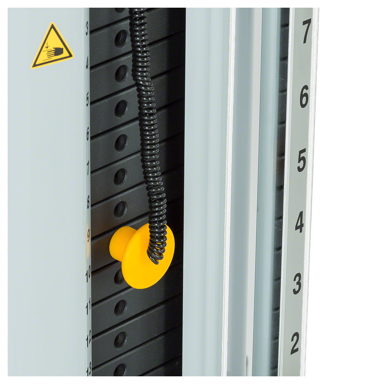 Close-up of the grey ‘ Lojer ’ double-pull mechanism with black weight plates. A yellow selection pin is inserted into one of the plates for weight adjustment. Next to it is a black coiled cable; scale 2–7. Yellow warning sign (risk of crushing).