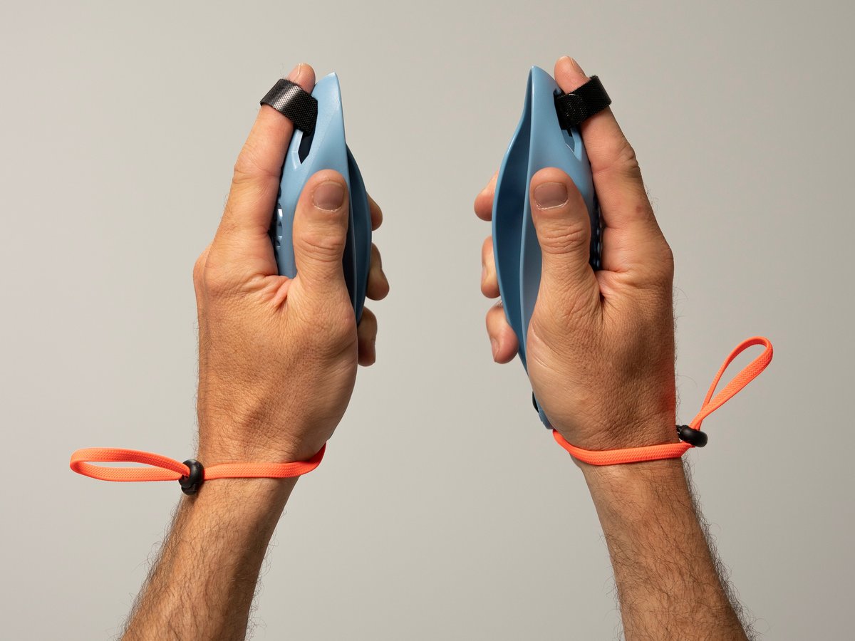 Deux mains tiennent une souris de course bleu clair. Un ruban noir la maintient à l'index, tandis que des rubans orange avec stoppeur entourent les poignets. Prise : index tendu, paumes légèrement vers l'extérieur.