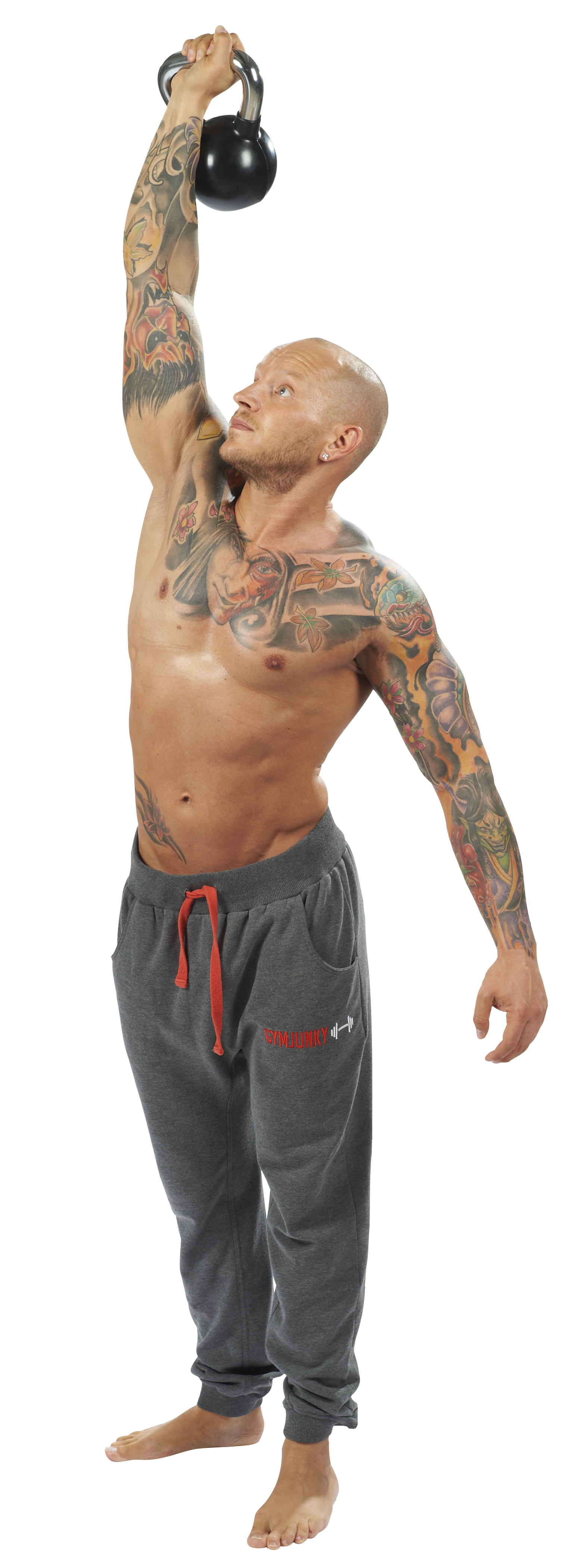 Un homme musclé, tatoué et au crâne rasé fait un exercice au-dessus de la tête avec un haltère sphérique noir. Il regarde l'haltère, la poignée chromée au-dessus de sa tête. Son jogging gris souligne l'effort.
