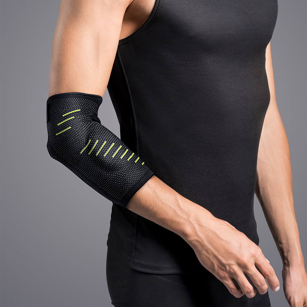 A sporty man is wearing a close-fitting black elbow support with neon-yellow stripes on his left arm. Breathable, fine-mesh fabric wraps around the elbow and provides support for conditions such as tennis elbow or osteoarthritis.