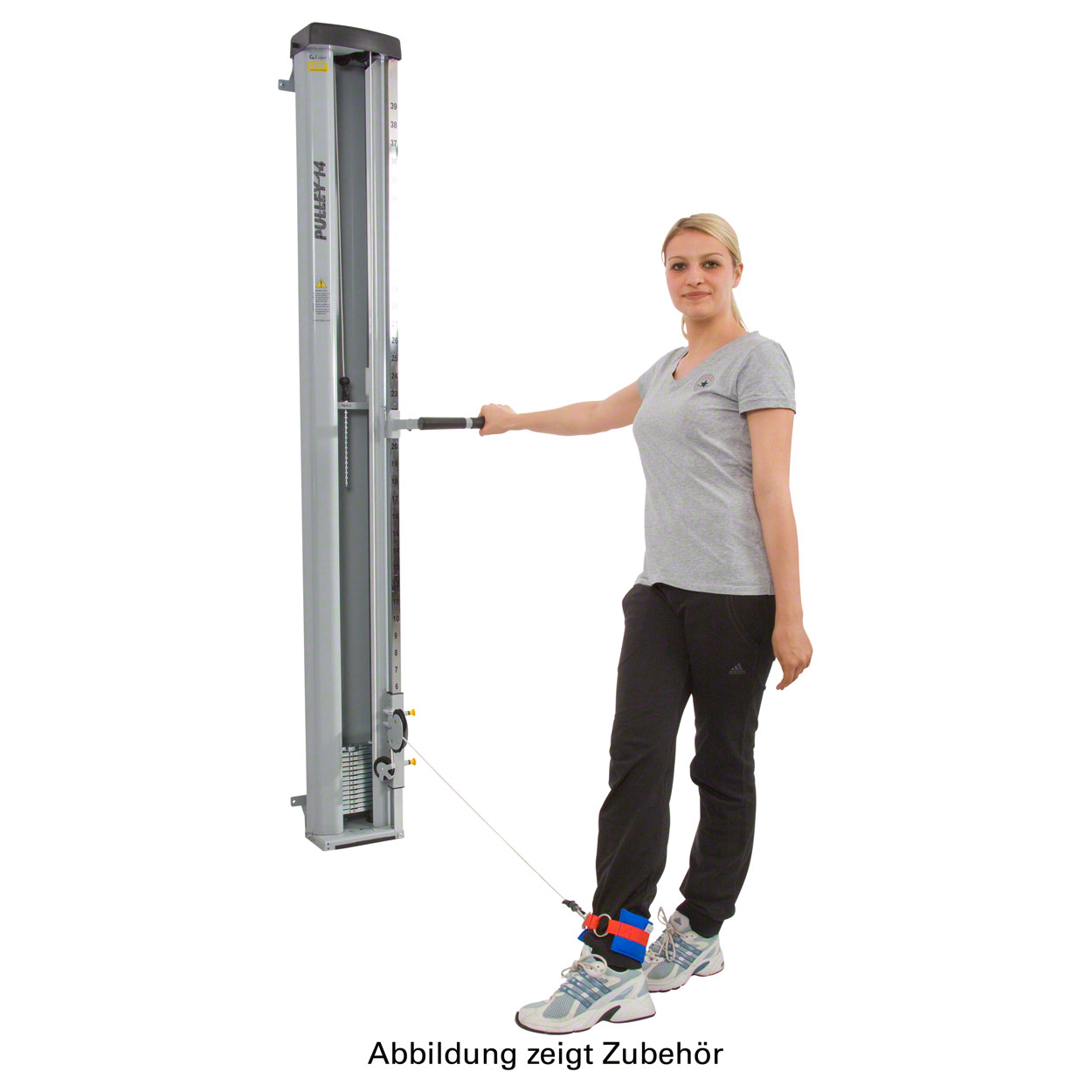 A blonde woman in sportswear performs a leg exercise on a grey cable machine. Holding the handle in her right hand, a red and blue strap on her left ankle is attached to the cable. This strengthens and improves leg mobility.