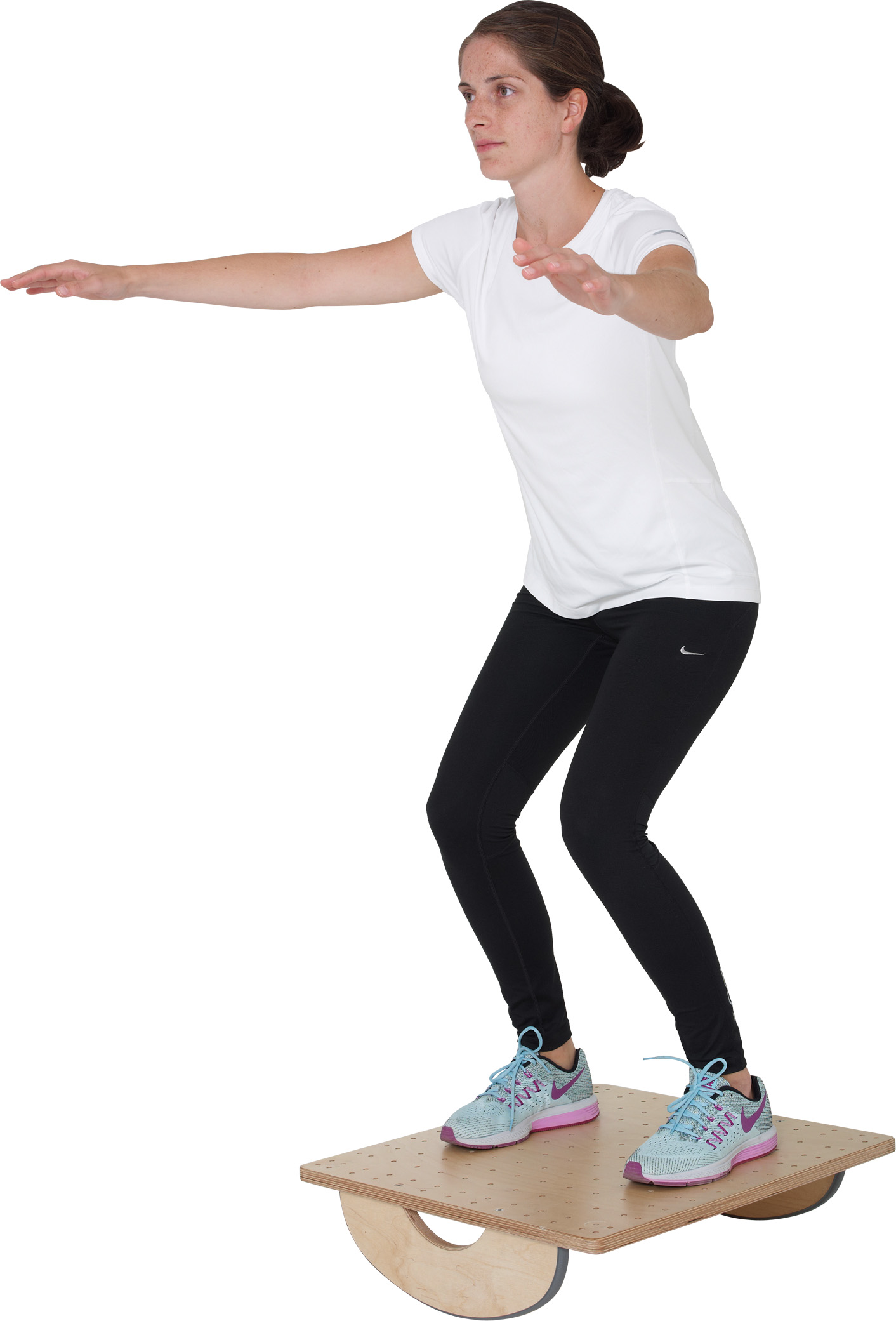 A young woman with dark hair, dressed in sportswear, is balancing on a Pedalo PT wobble board whilst in a slight squat. She is holding her arms out to the sides to maintain her balance on the light-coloured wooden board.