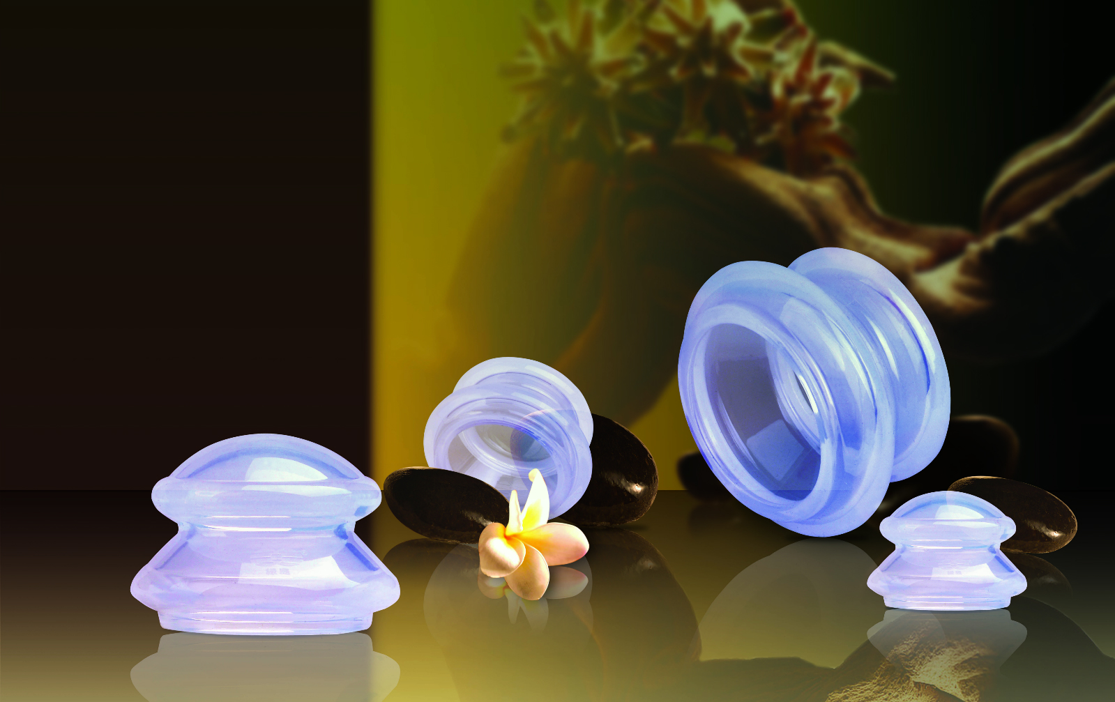 Quattro coppette in silicone blu trasparente di varie dimensioni su una superficie scura e riflettente. Le forme flessibili sono visibili. Tra esse, un fiore giallo chiaro e oggetti ovali scuri. Sfondo giallo-verde sfocato.
