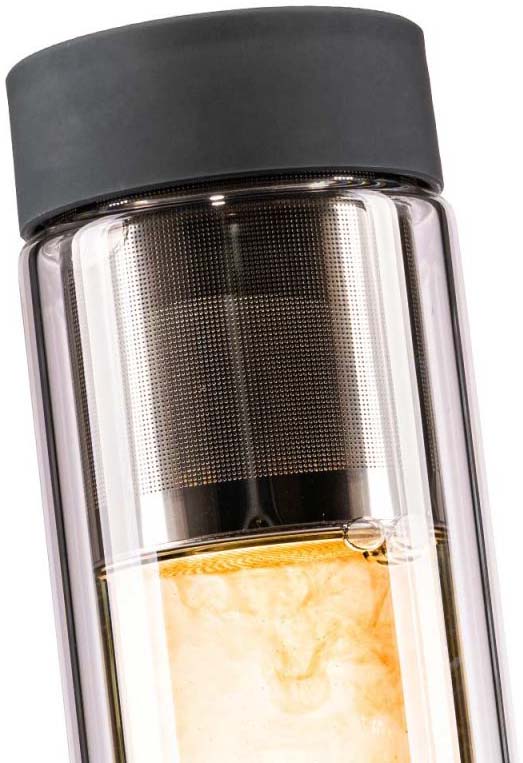 Primo piano di una borraccia in vetro a doppia parete con tappo in silicone scuro. All’interno si vede un colino in acciaio finemente forato con tè sfuso che colora l’acqua di oro chiaro. Bollicine salgono nell’infuso ambra.