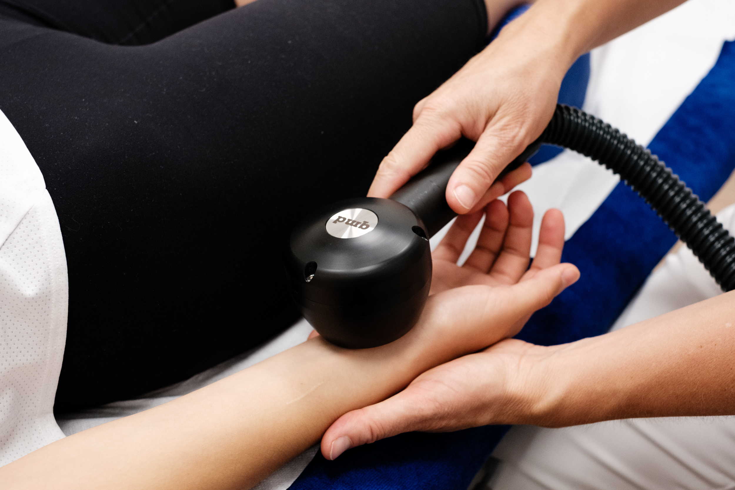 Nahaufnahme einer therapeutischen Behandlung am Unterarm. Eine Hand hält ein schwarzes qmd
®
cryo-thermal Gerät, das auf den Arm einer liegenden Person angewendet wird, um gezielt Kälte- oder Wärmetherapie zu spenden. Das Gerät zeigt das qmd-Logo.