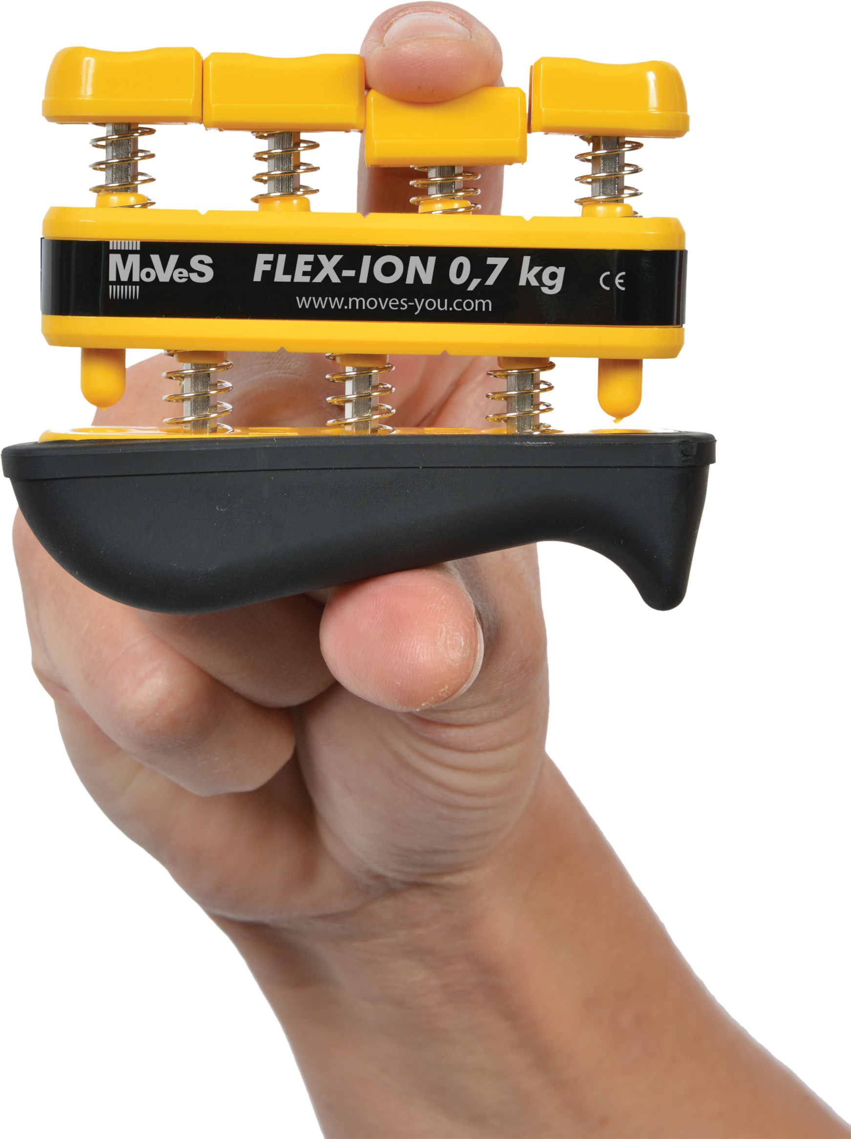 A hand is holding a yellow and black Moves Flex-Ion hand trainer. The index finger is pressing one of the four yellow, spring-loaded buttons, demonstrating controlled finger strengthening. Labelled: ‘FLEX-ION 0.7 kg’.