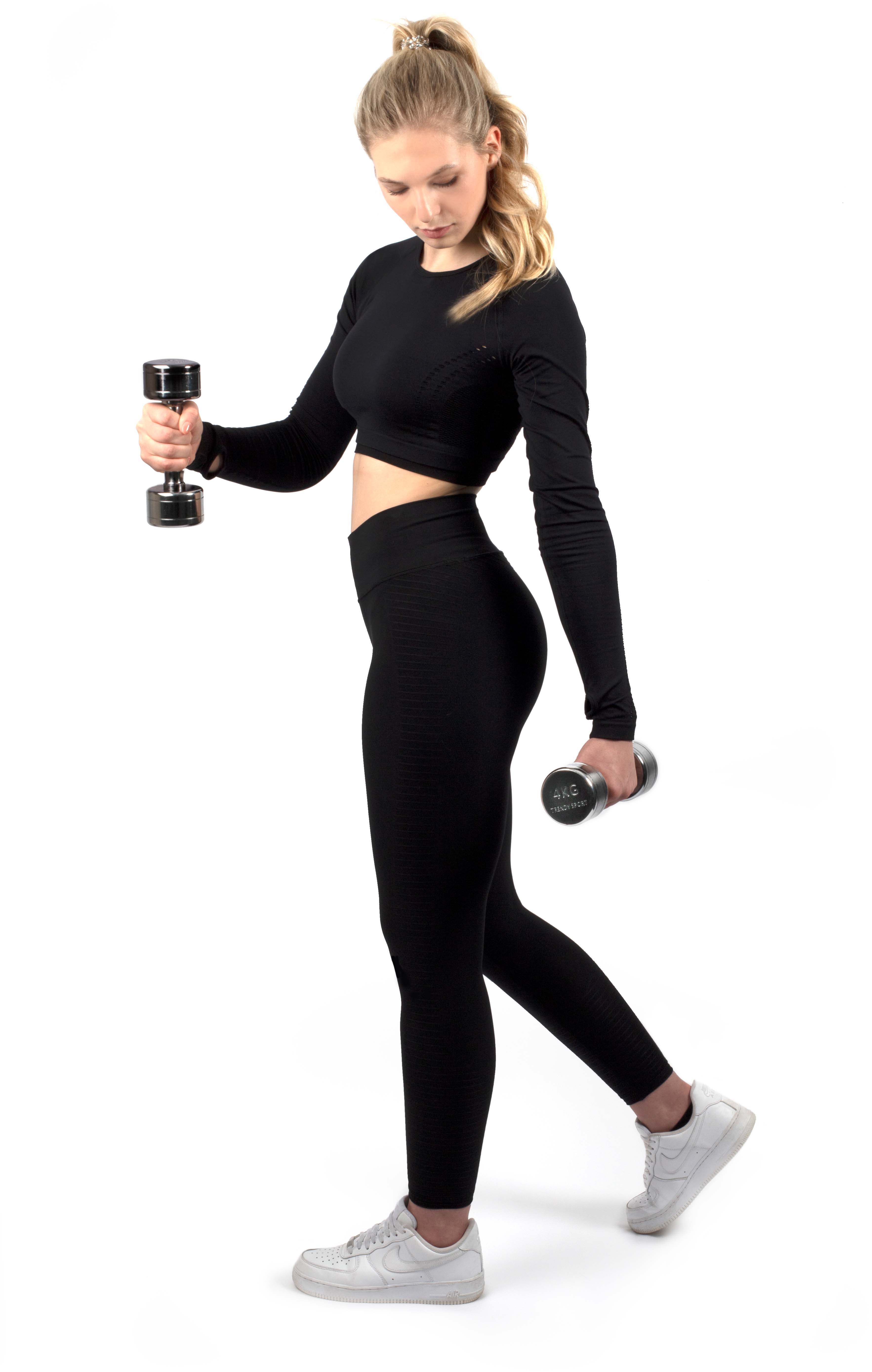 Jeune femme blonde en queue de cheval, portant un haut de sport noir court et un legging, sur fond blanc. Elle tient deux haltères chromés à poignée striée ; sur celui de gauche : « 4 kg Trendy Sport ». Pose d’exercice.